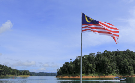 Malaysia flag jalur gemilang waving with the background of boat at the lake and malaysian rainforest trees Stock Photo