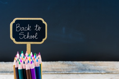 Wooden mini blackboard label with message back to school and colouring pencils over chalkboard background copy space available education concept