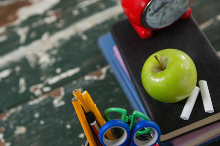 Close up of alarm clock apple and chalk on stack of books with pen holder Stock Photo