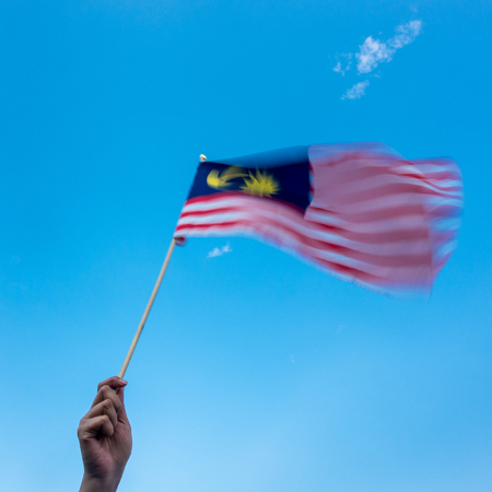 Hand holding malaysia flag wind blowing motion blur on flag blue sky