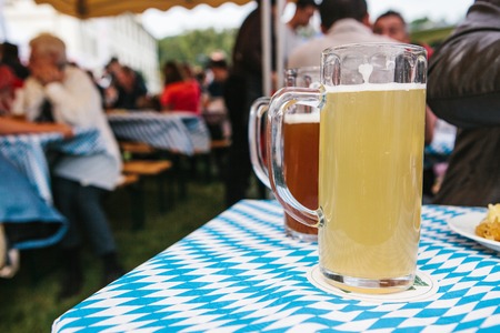 Two mugs with a light and dark beer stand on the table in the background blurred people celebrating the traditional german beer festival called oktoberfest